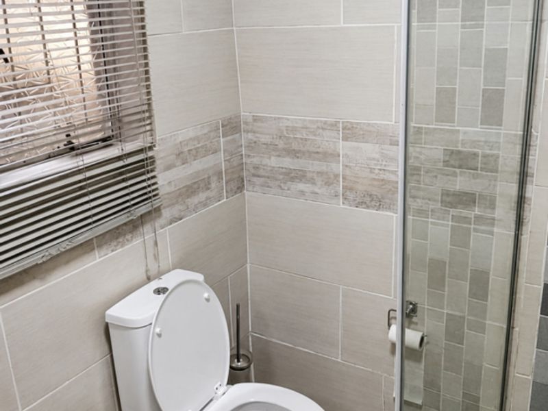 A modern bathroom featuring neutral wall and floor tiling, a glass-enclosed shower, and a window with fitted blinds.