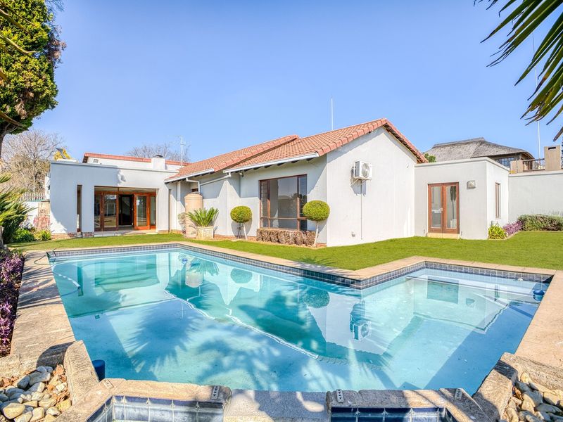 A well-maintained rear garden featuring a swimming pool with stone coping, set against the back elevation of the house with a tiled roof.
