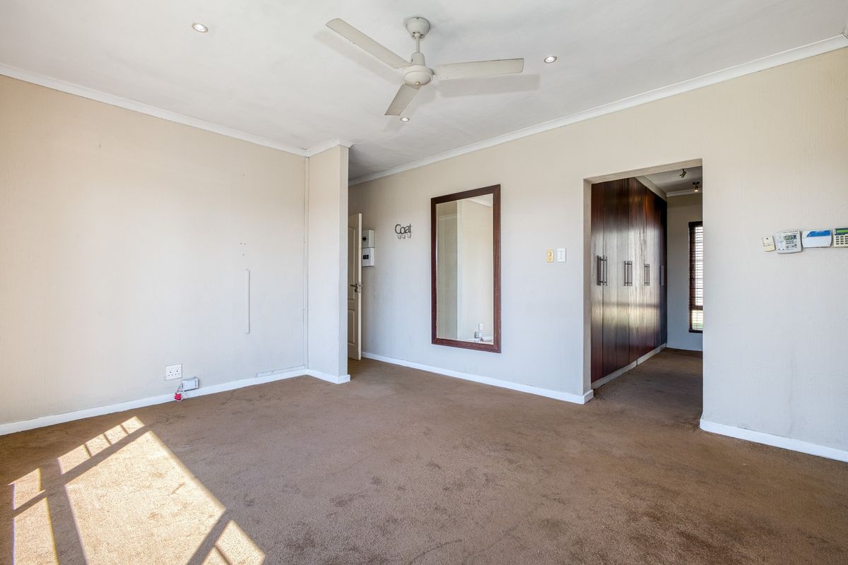 Spacious bedroom featuring neutral walls, carpet flooring, a ceiling fan, and built-in cupboards with access to an adjoining dressing area.