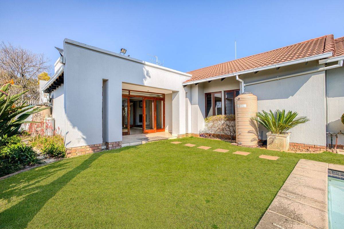 Rear view of the property featuring a landscaped lawn, paved stepping stones, a water storage tank, and access to the interior via sliding doors.