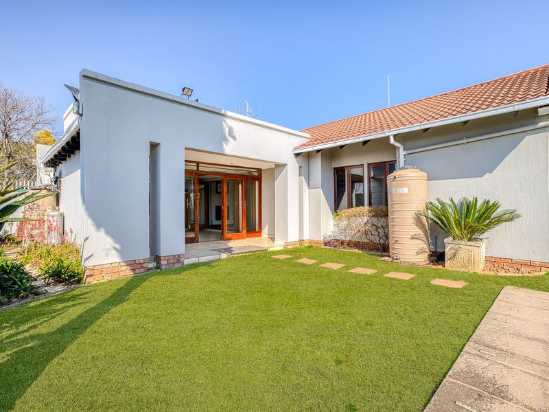 Rear view of the property featuring a landscaped lawn, paved stepping stones, a water storage tank, and access to the interior via sliding doors.