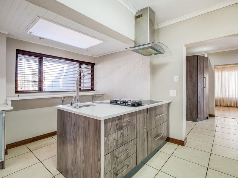 A modern kitchen featuring a central island with a gas hob, extractor fan, and undermount sink, complemented by tiled flooring and a skylight.