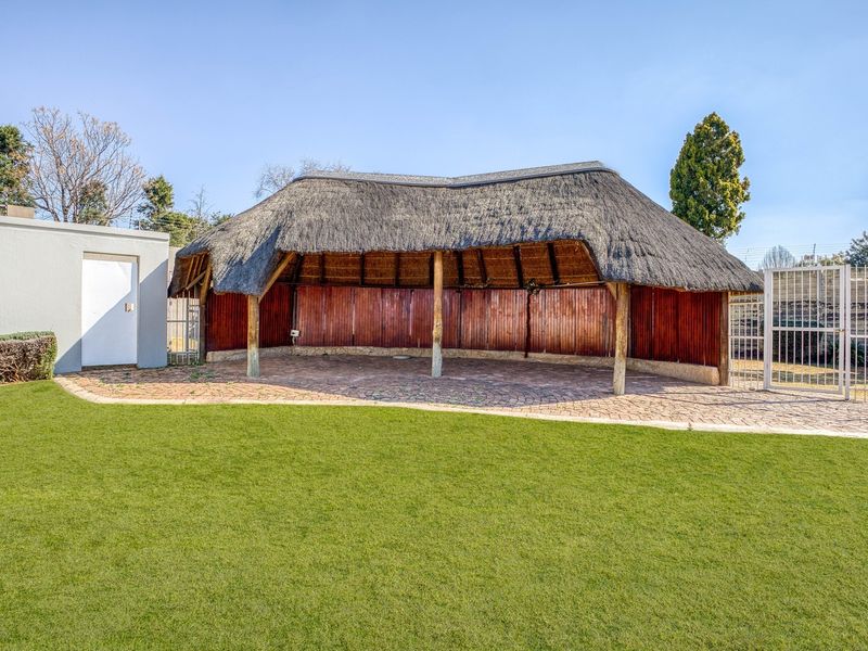 A spacious outdoor thatched lapa area featuring paved flooring and timber wall cladding, perfect for garden entertaining.