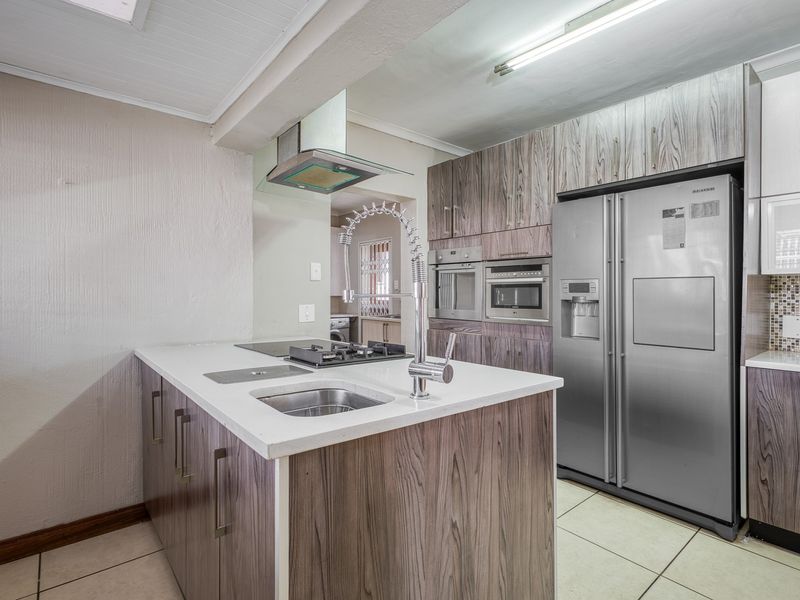 Modern kitchen featuring a central island with a gas hob and sink, built-in appliances, and wood-grain cabinetry with ample storage space.