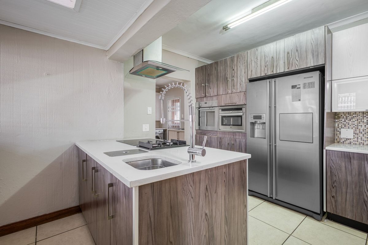 Modern kitchen featuring a central island with a gas hob and sink, built-in appliances, and wood-grain cabinetry with ample storage space.