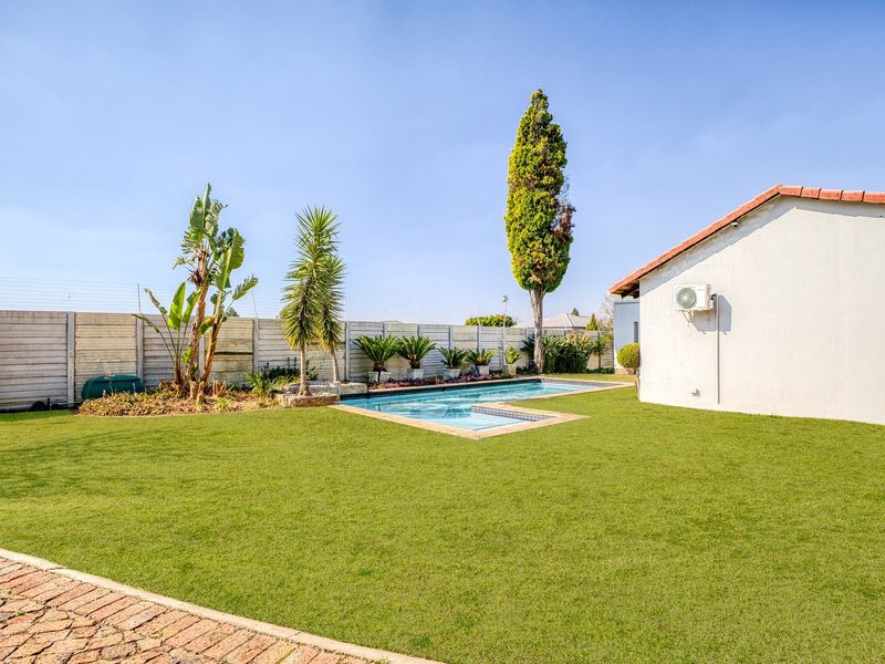 A well-maintained backyard featuring a swimming pool, manicured lawn, and secure perimeter walling with electric fencing.