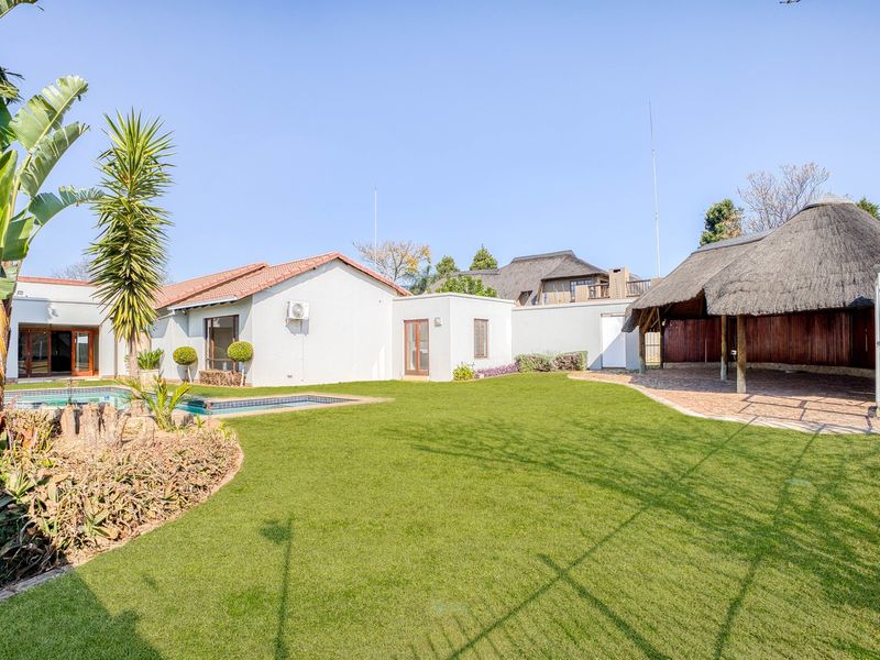 Spacious rear garden featuring a swimming pool, a large thatched lapa for outdoor entertaining, and a well-maintained artificial lawn area.