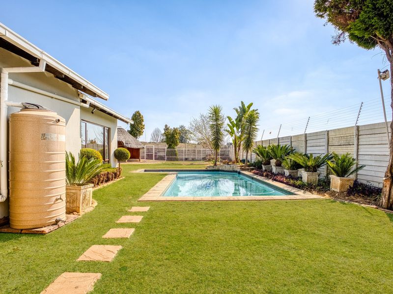 A well-maintained backyard featuring a swimming pool, paved surround, lawn area, and a large water storage tank attached to the house exterior.