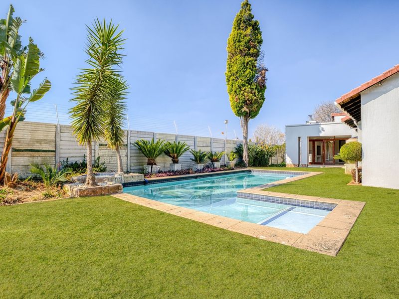 A well-maintained outdoor pool area featuring a clear swimming pool, manicured lawn, and secure boundary wall, providing a private space for relaxation.