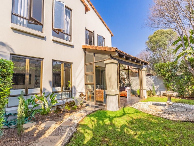 Rear view of the property featuring a covered patio, landscaped garden with stone pathways, and established trees.