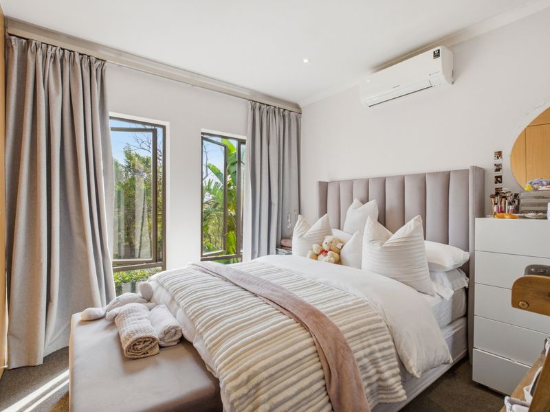 A well-maintained bedroom featuring built-in cupboards, an air conditioning unit, and large windows allowing for natural light.