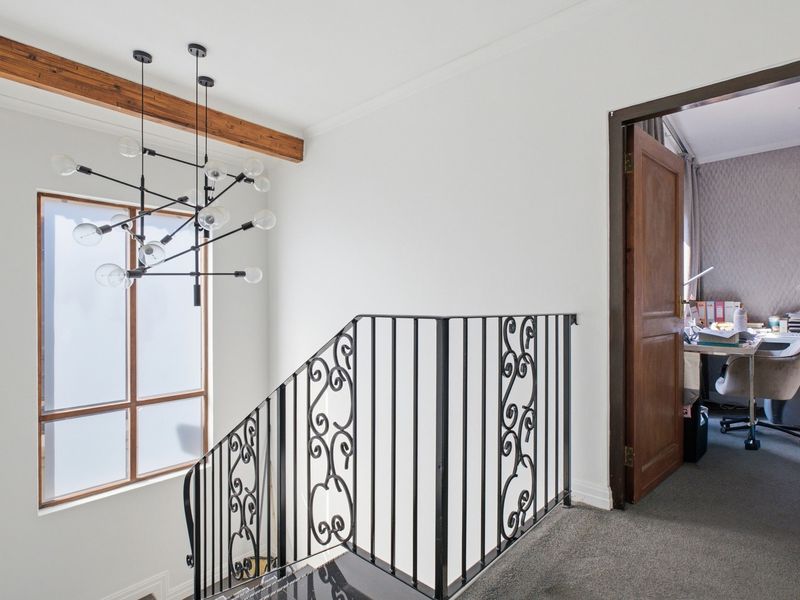 A bright landing area featuring a decorative wrought iron balustrade, exposed timber beam, and a modern chandelier, leading into an adjacent room.