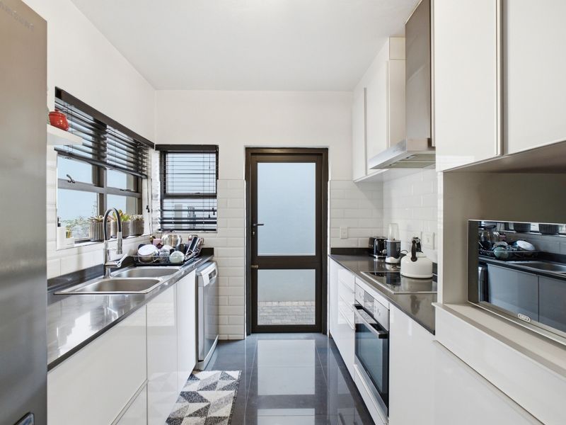 A modern, well-maintained galley kitchen featuring sleek white cabinetry, dark stone countertops, subway tile backsplash, and integrated stainless steel appliances.