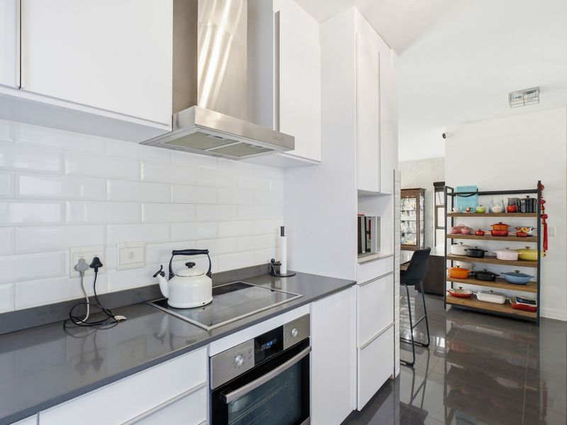 Modern kitchen featuring sleek white cabinetry, quartz countertops, subway tile backsplash, and integrated stainless steel appliances, flowing into an open-plan living area.