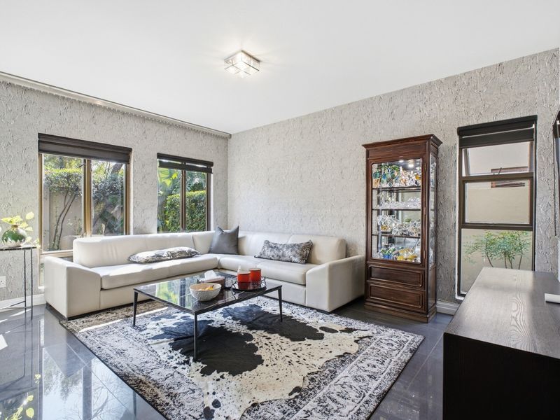 A well-maintained living room featuring textured wall finishes, large windows with roller blinds, and polished dark floor tiles.