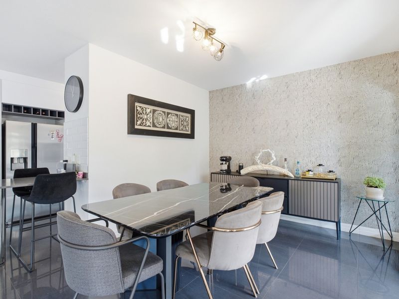 Modern open-plan dining area featuring sleek tiled flooring, a textured feature wall, and an integrated breakfast bar adjacent to the kitchen space.