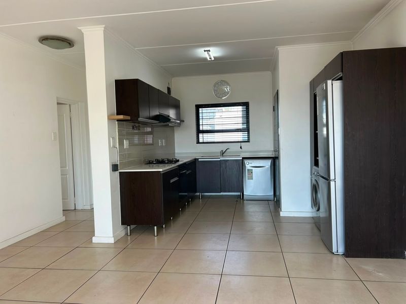 A functional kitchen featuring dark wood cabinetry, tiled flooring, a gas hob, and integrated appliances, offering a clean and practical workspace.