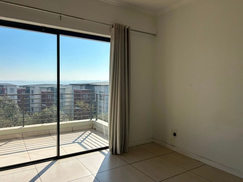 An empty living area featuring large sliding glass doors that open onto a balcony with neighborhood views and tiled flooring throughout.