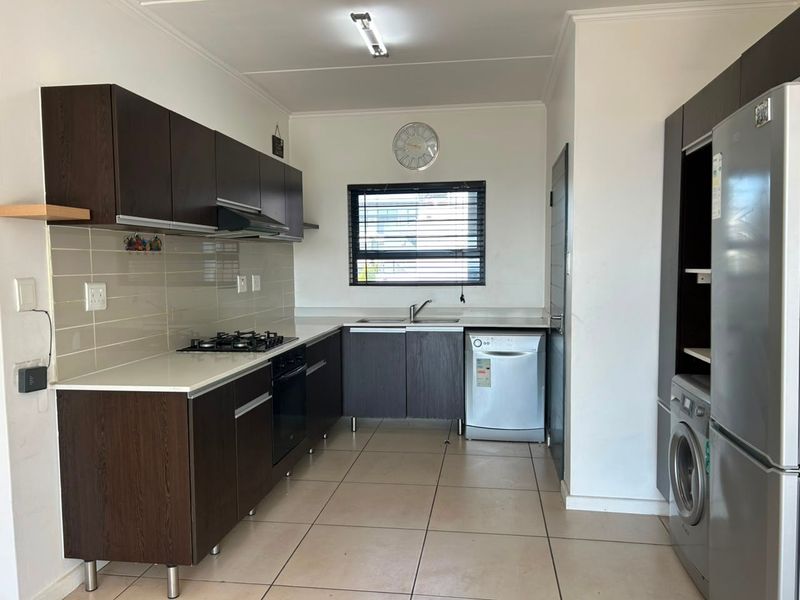 Modern kitchen featuring dark wood cabinetry, gas hob, electric oven, extractor fan, tiled backsplash, and neutral floor tiles.