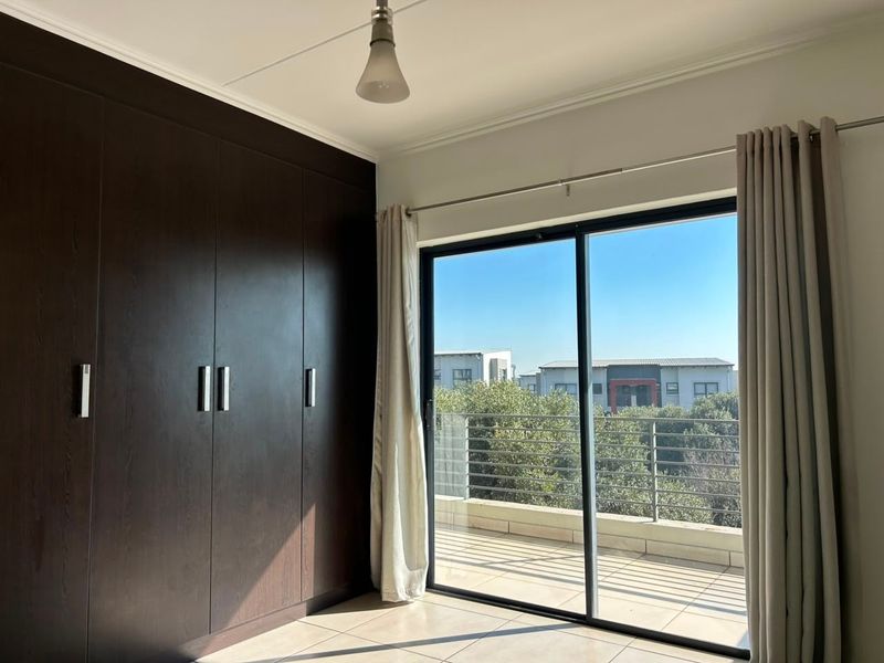 A bright, empty bedroom featuring dark wood built-in cupboards, tiled flooring, and a sliding glass door providing direct access to a private balcony.