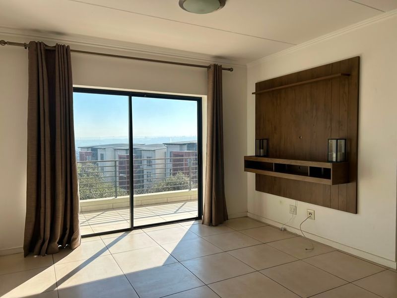 Bright living room featuring large sliding glass doors leading to a balcony, tiled flooring, and a built-in wooden wall unit.