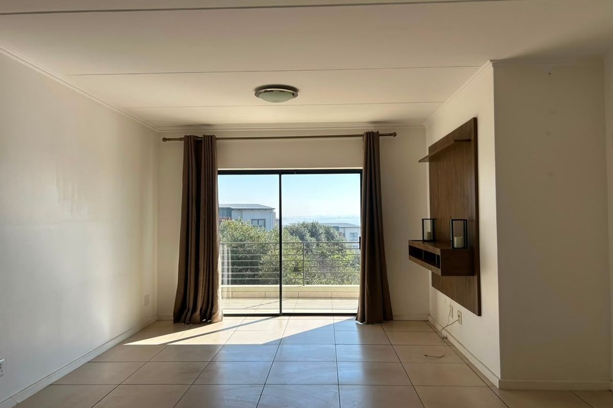 Spacious living area featuring neutral tiled flooring, a built-in wall unit, and large sliding glass doors leading to a balcony with scenic views.
