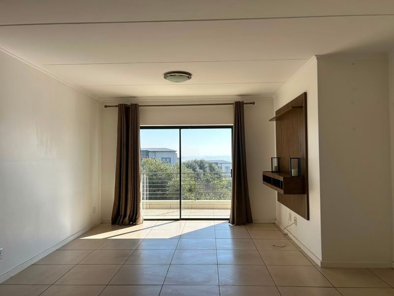 Spacious living area featuring neutral tiled flooring, a built-in wall unit, and large sliding glass doors leading to a balcony with scenic views.