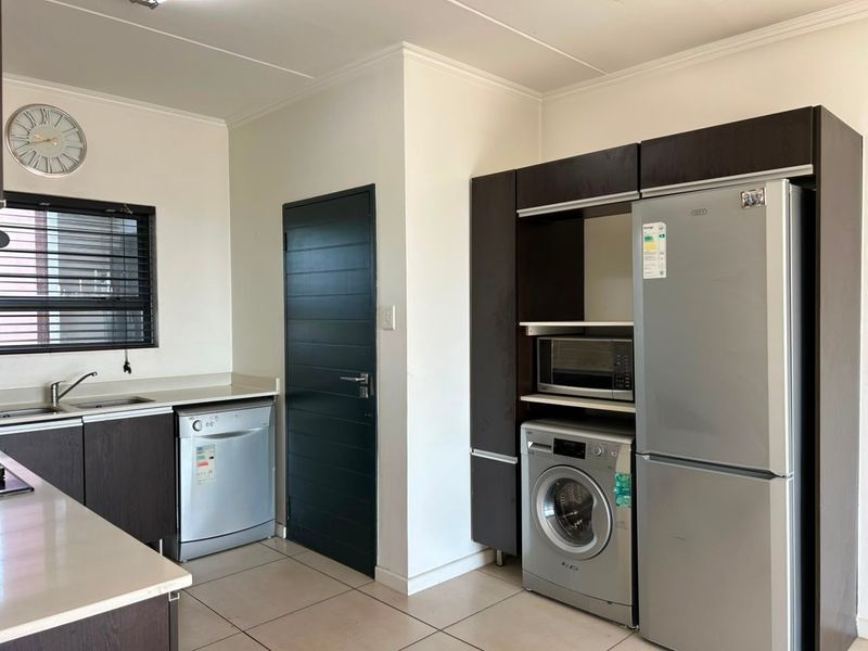 A functional kitchen featuring dark wood cabinetry, stone countertops, tiled flooring, and integrated spaces for appliances including a washing machine and refrigerator.