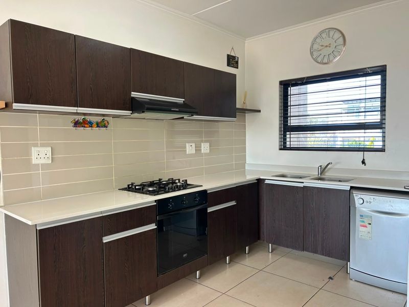 A functional kitchen featuring dark wood cabinetry, a gas hob, built-in oven, extractor fan, tiled backsplash, and a double sink with tiled flooring.
