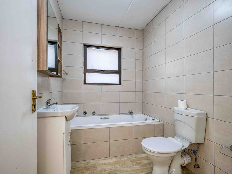 A functional bathroom featuring a built-in bathtub, vanity basin, and toilet, finished with neutral ceramic wall and floor tiles.