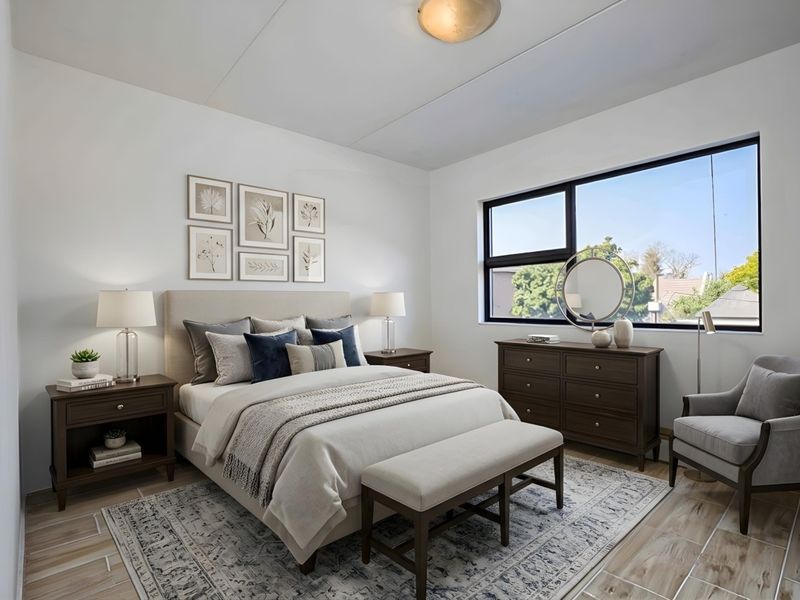 A well-lit, modern bedroom featuring large windows, neutral walls, and tiled flooring, creating a bright and comfortable living space.