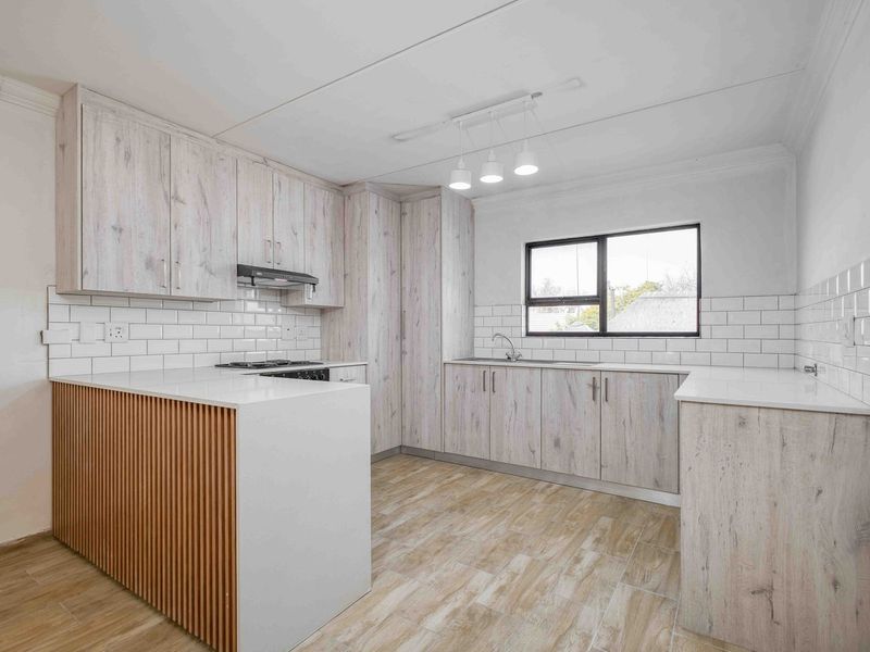 Modern kitchen featuring light wood-grain cabinetry, white stone countertops, subway tile backsplash, and a functional breakfast bar island.