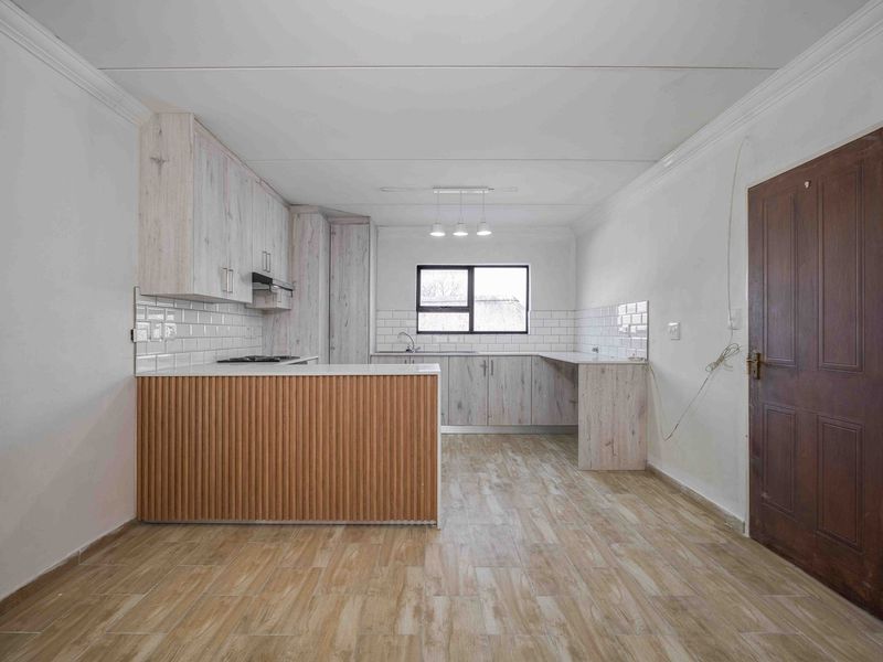 A clean, modern kitchen featuring light wood-look cabinetry, subway tile backsplash, a built-in hob, and wood-effect floor tiles in an open-plan layout.