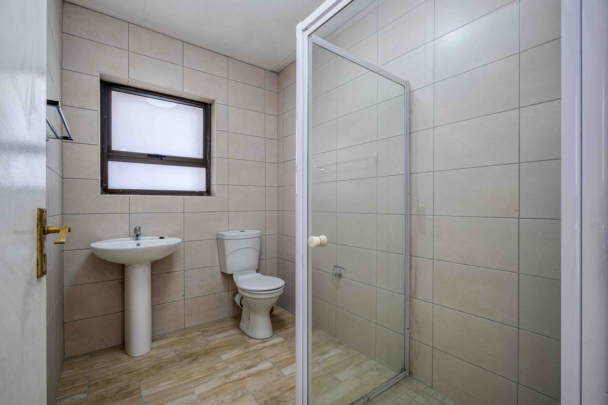 A clean, functional bathroom featuring a pedestal basin, toilet, and a glass-enclosed shower with neutral wall and floor tiling.