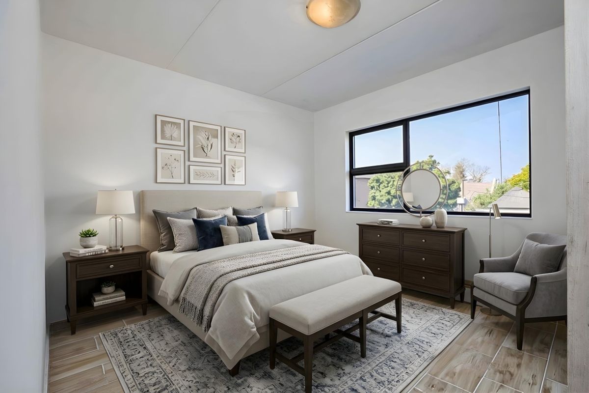 A well-lit, modern bedroom featuring large windows, neutral walls, and tiled flooring, creating a bright and comfortable living space.