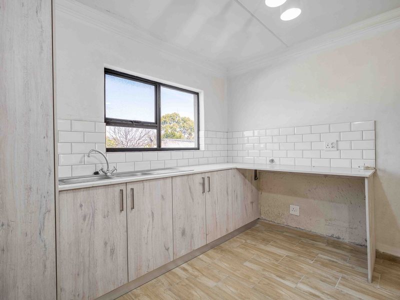 A clean, modern kitchen featuring light wood-look cabinetry, subway tile backsplash, and wood-look tile flooring, with an unfinished section under the counter.