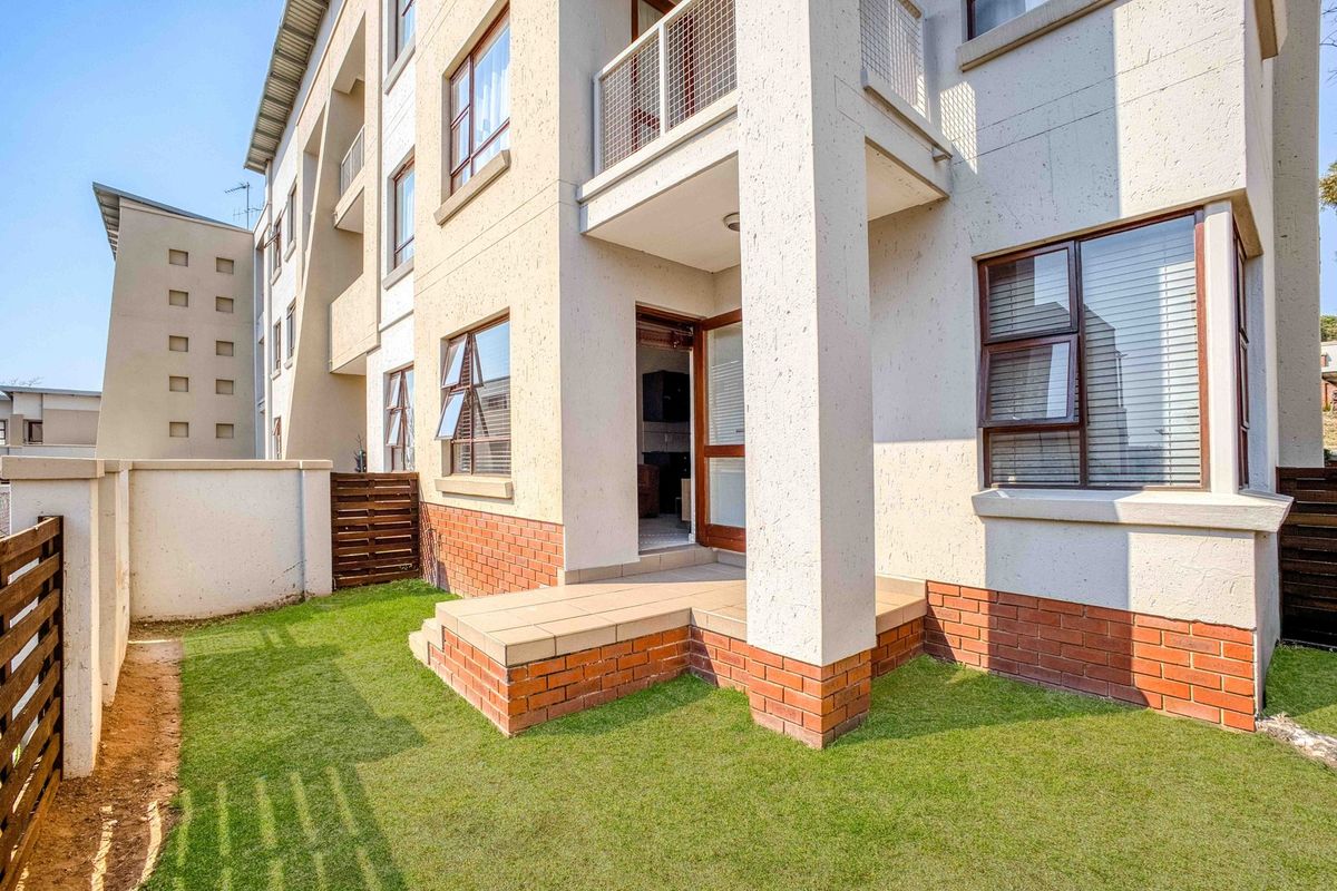 Rear view of the apartment building featuring a ground floor tiled patio, small private garden area, and upper-level balconies with aluminium window frames.