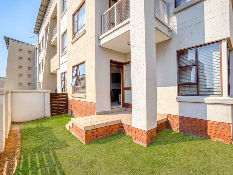 Rear view of the apartment building featuring a ground floor tiled patio, small private garden area, and upper-level balconies with aluminium window frames.