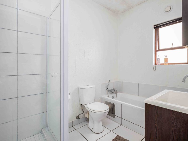 A functional bathroom featuring a separate shower enclosure, bathtub, toilet, and vanity basin with tiled finishes throughout.