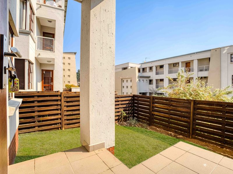 A private ground-floor patio area featuring tiled flooring, artificial grass, and timber slat fencing, providing a compact outdoor space for the apartment.