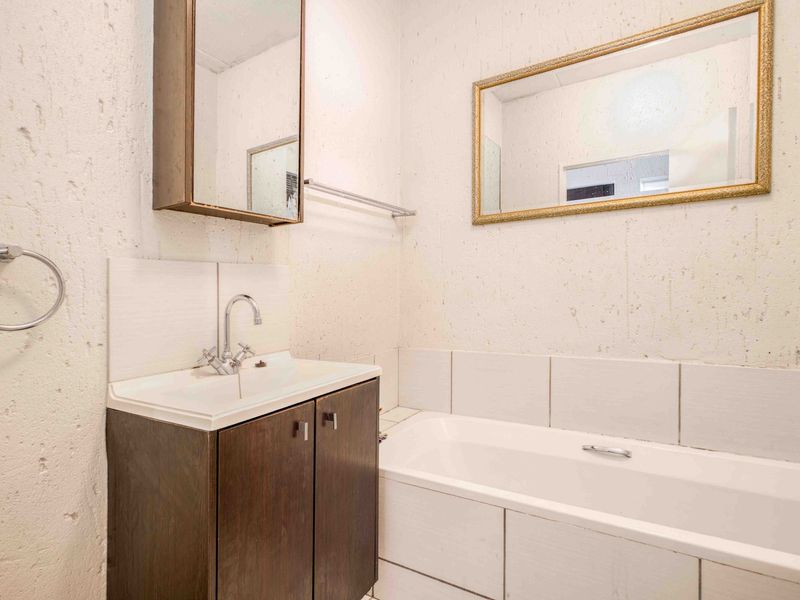 A compact bathroom featuring a vanity with basin, bathtub, and wall-mounted medicine cabinet, requiring cosmetic updates to the wall finishes.