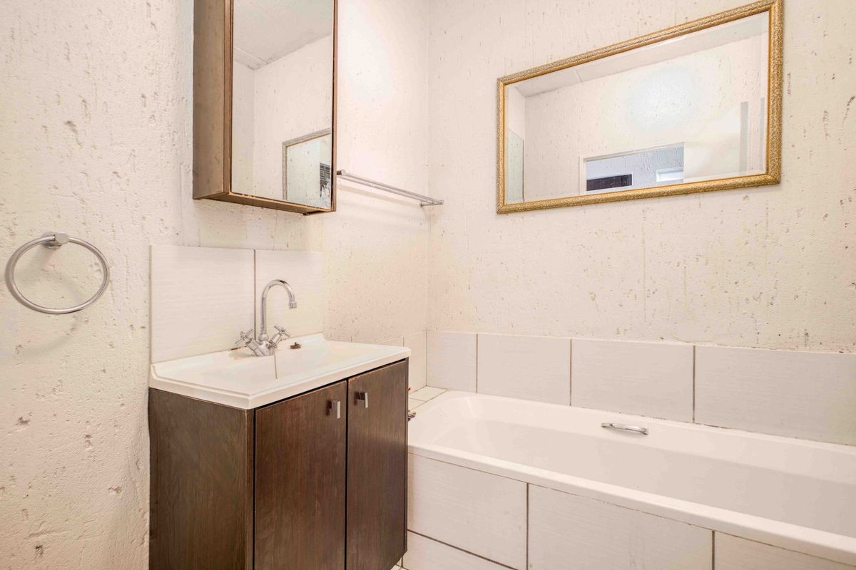 A compact bathroom featuring a vanity with basin, bathtub, and wall-mounted medicine cabinet, requiring cosmetic updates to the wall finishes.