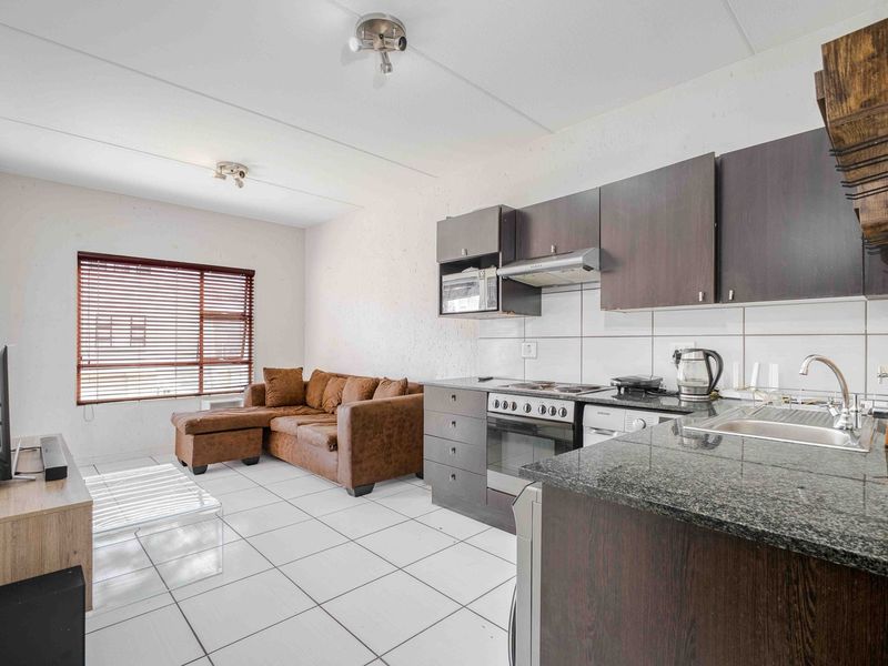 Open-plan living area featuring a compact kitchen with granite countertops, built-in oven, hob, and tiled flooring throughout.