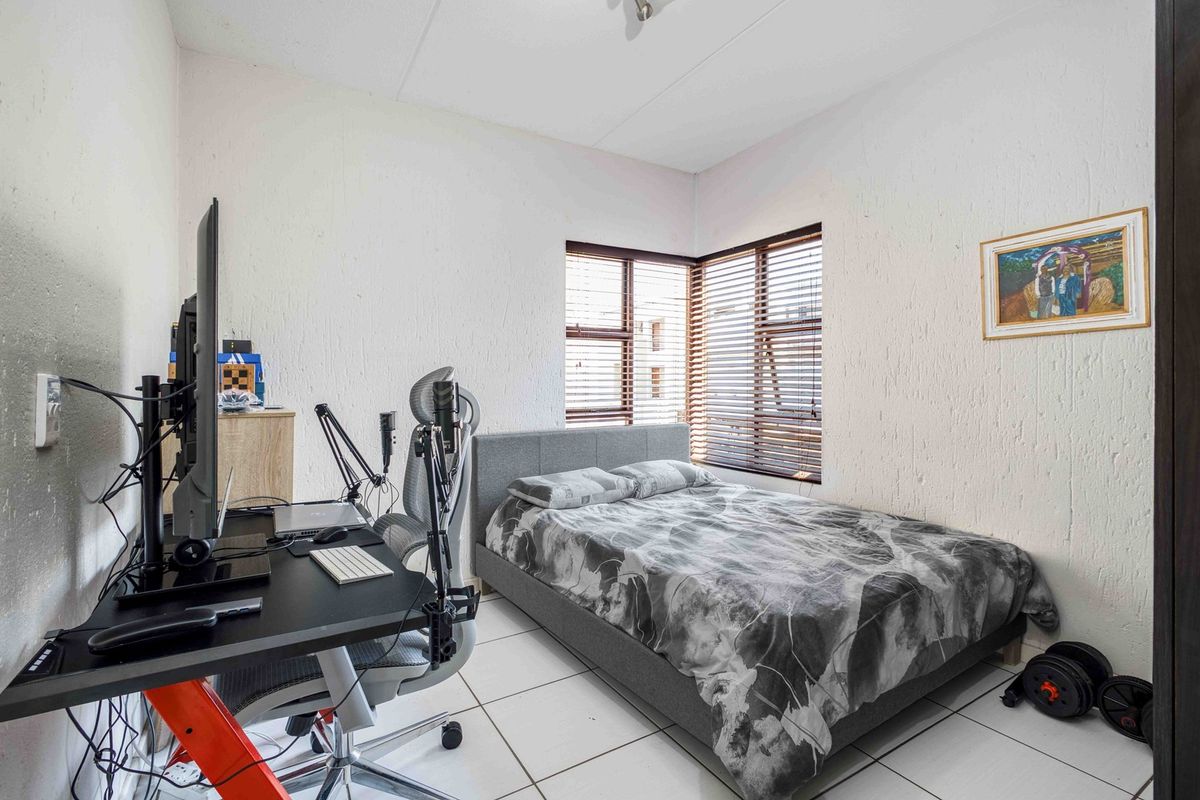 A functional bedroom featuring tiled flooring and a corner window with fitted venetian blinds, providing natural light and a compact layout.