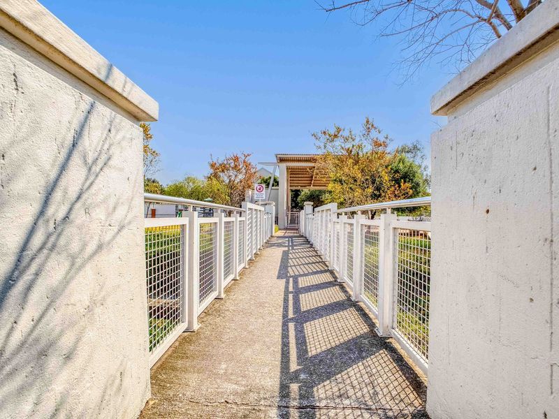 A pedestrian bridge walkway featuring concrete paving and metal railings, providing access to the property entrance.