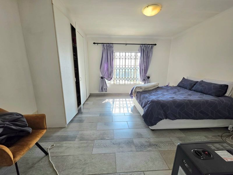 A bedroom featuring tiled flooring, built-in cupboards, and a window fitted with a security gate.
