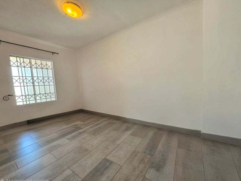 A bright, empty bedroom featuring neutral tiled flooring, a security gate on the window, and a simple ceiling light fixture.
