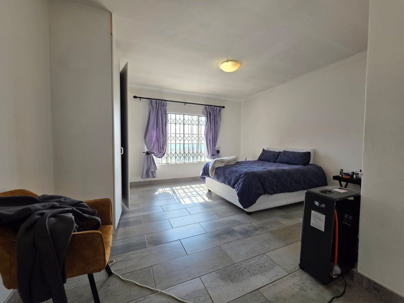 Spacious bedroom featuring tiled flooring, built-in cupboards, and a security gate on the window, offering a functional and well-lit living space.