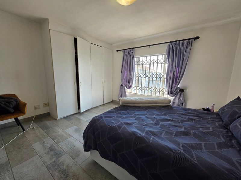 A bedroom featuring tiled flooring, built-in cupboards, and a window fitted with a security gate.