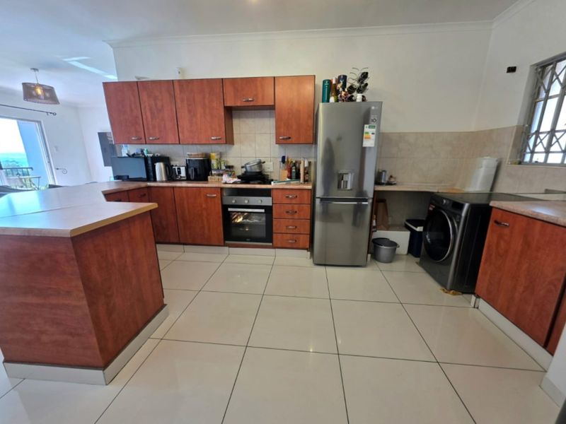 A functional kitchen featuring wood-finish cabinetry, laminate countertops, tiled flooring, and integrated appliances, with an open-plan layout leading to the living area.
